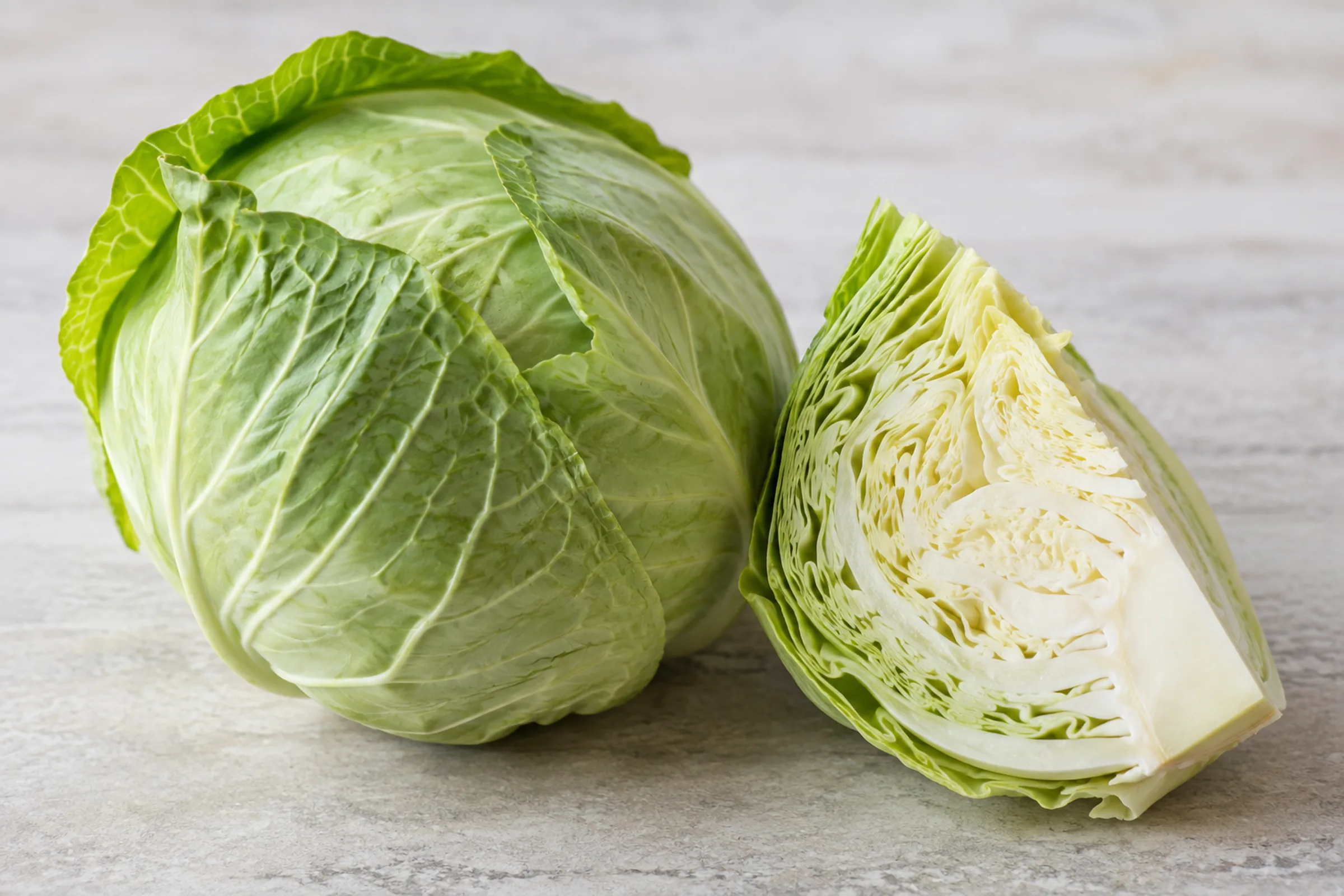 A whole green cabbage with one wedge cut open showing its layered leaves